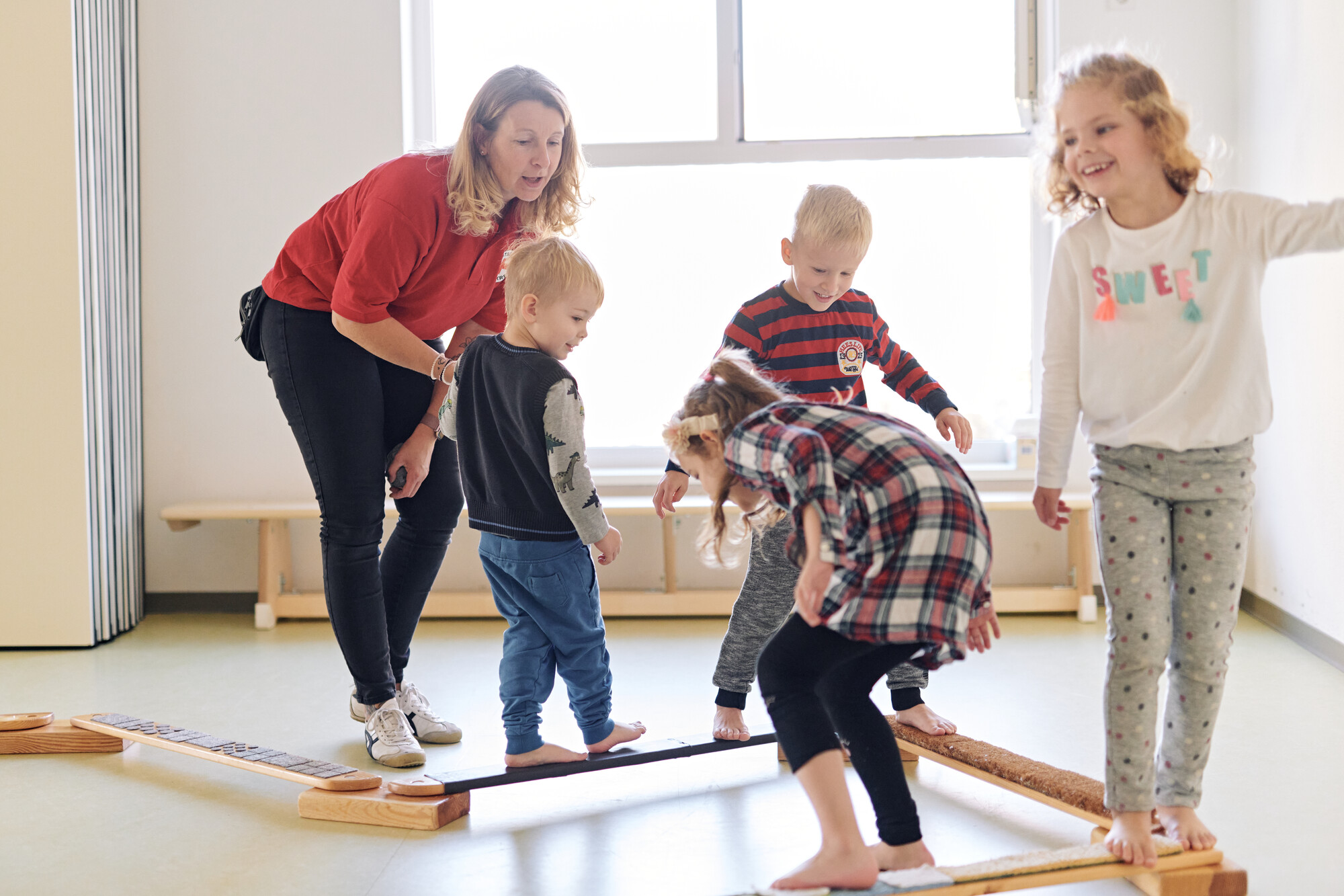DRK Mitarbeiterin leitet vier Kinder an beim Balancieren im Gymnastikraum