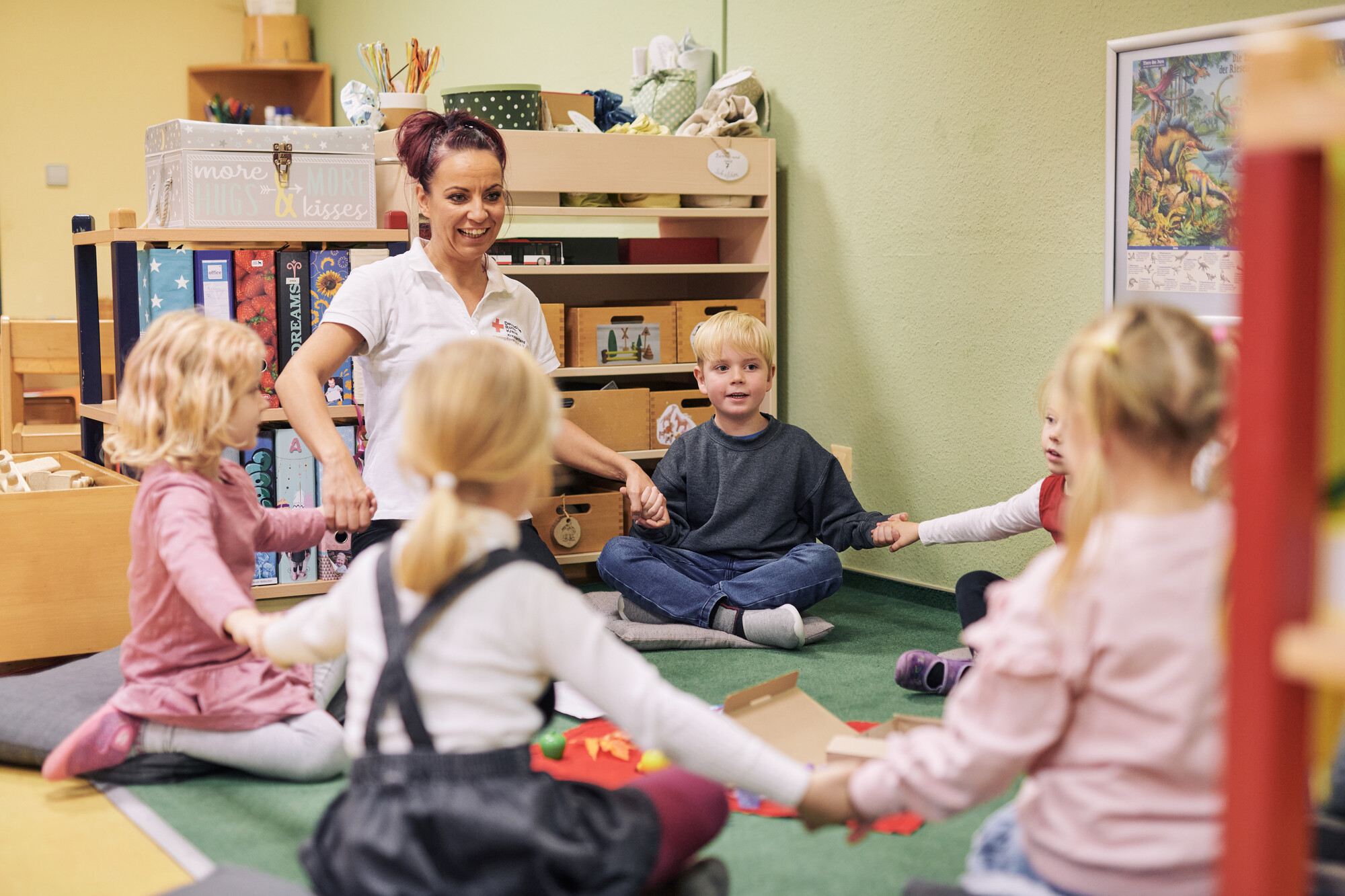 Kinder beim Spiel mit einer Erzieherin, alle fassen sich an den Händen