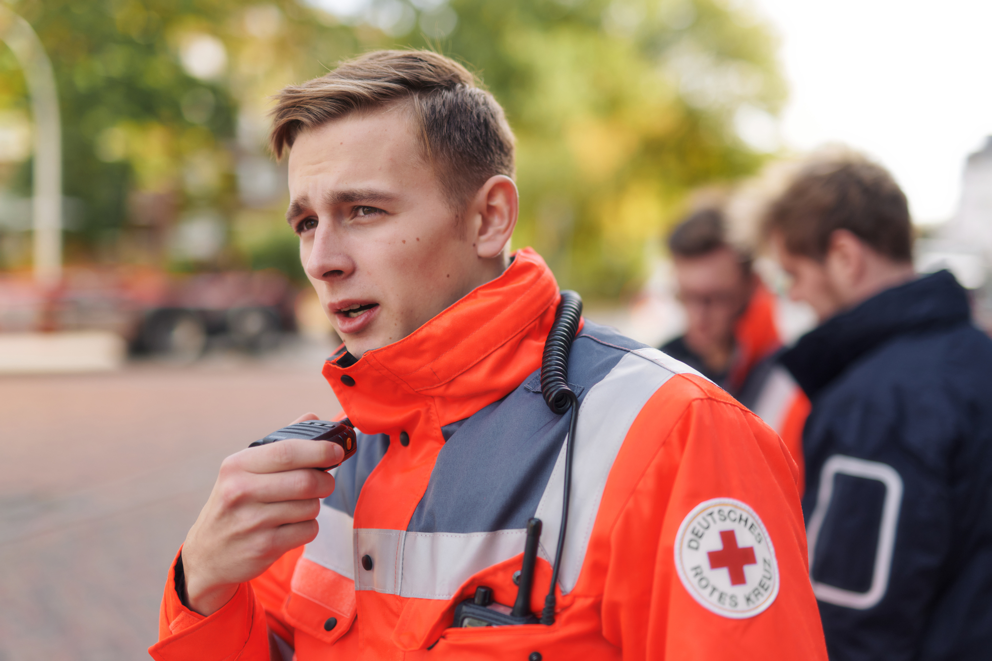 Symbolfoto, Mitarbeiter des DRK in Einsatzjacke spricht in ein Funkgerät