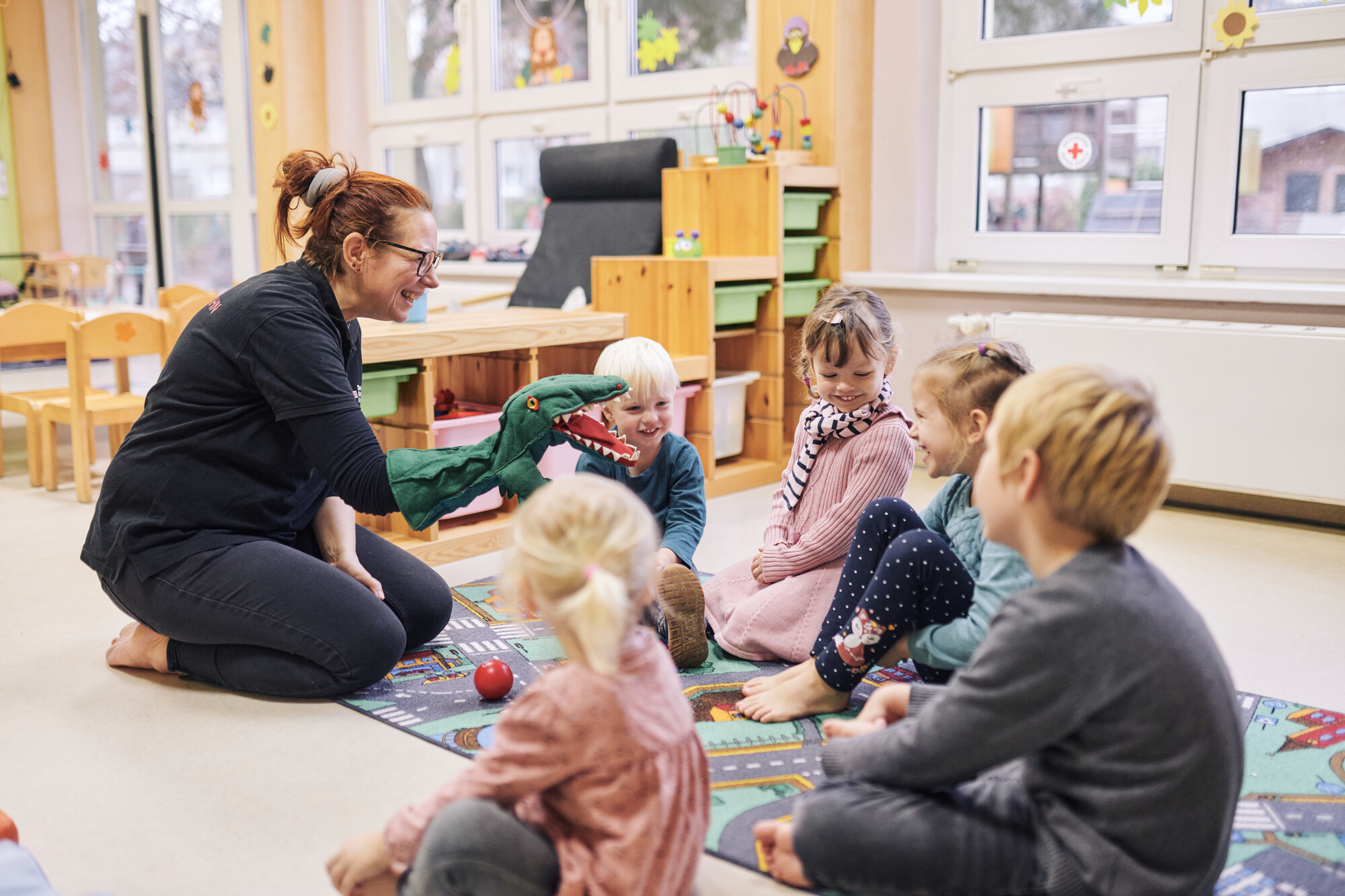 Erzieherin spielt mit einer Handpuppe (ein Dinosaurier) vor einer Gruppe Kinder