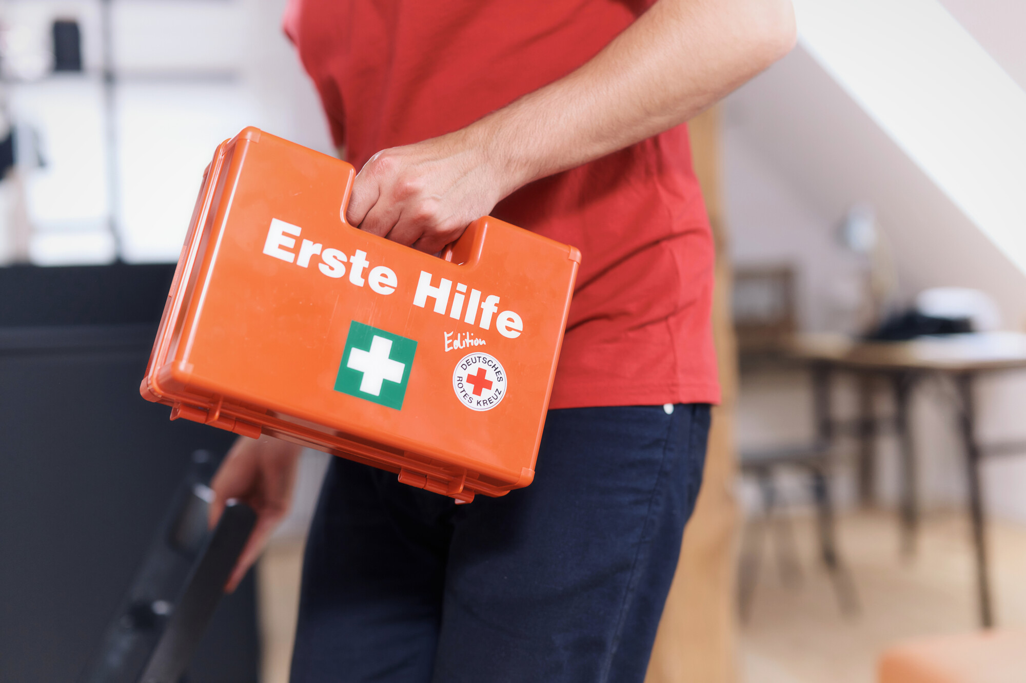 Erste Hilfe Situation: Versorgung einer Schnittwunde an der Hand, die sich eine Frau beim Gemüseputzen in der Küche zugezogen hat. Der Mann kommt mit dem Erste-Hilfe-Koffer