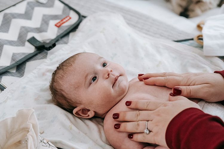 Baby liegt mit Windel auf Wickeltisch, während Mutter es streichelt