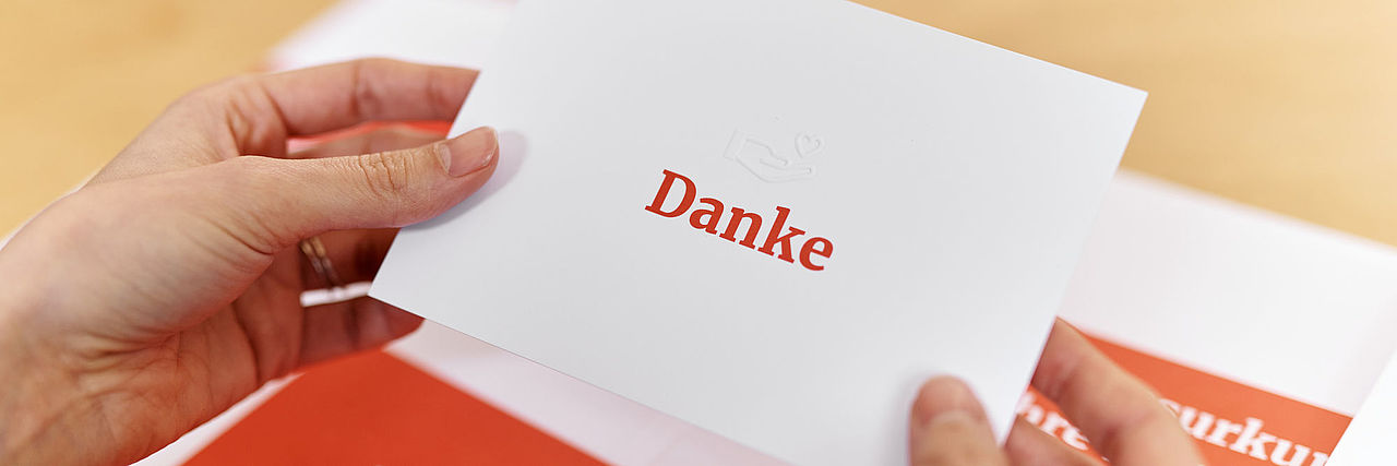Symbolfoto Mappe mit Dokumenten des DRK (Dankesurkunde). Hände halten eine Karte mit einer Danksagung