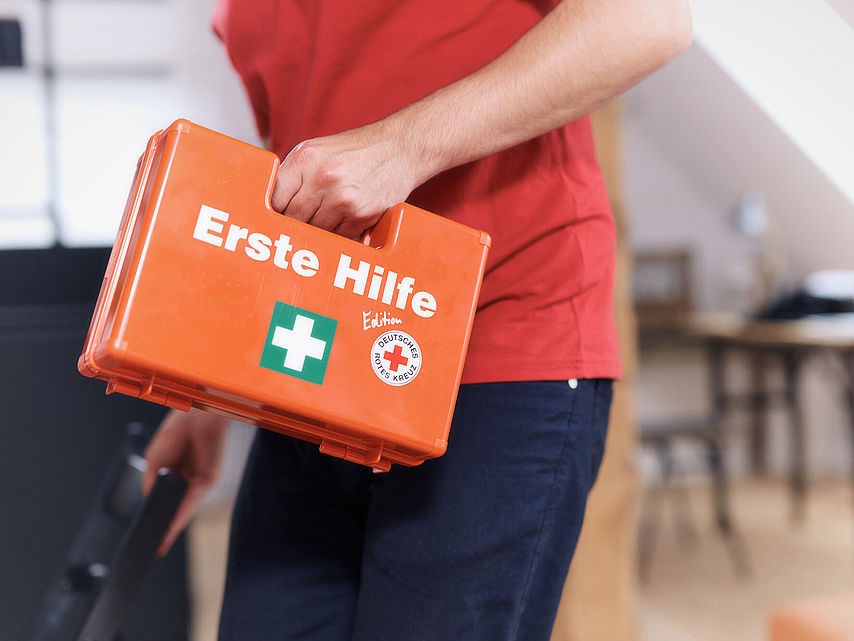 Erste Hilfe Situation: Versorgung einer Schnittwunde an der Hand, die sich eine Frau beim Gemüseputzen in der Küche zugezogen hat. Der Mann kommt mit dem Erste-Hilfe-Koffer