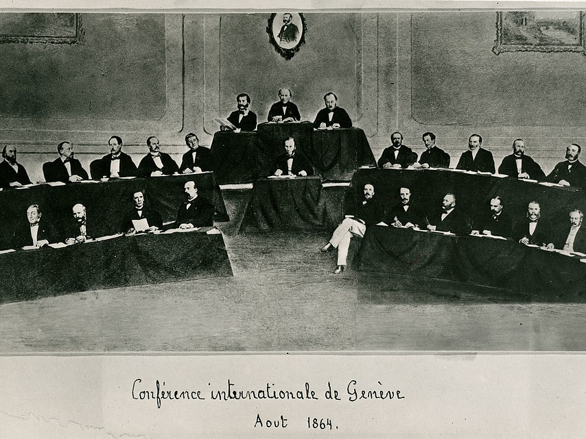 Zweite Genfer Konferenz, auf der die Erste Genfer Konvention unterzeichnet wurde: die Delegierten und der Vorsitzende Guillaume Dufour (oben Mitte). Über ihm hängt ein Portrait von Henry Dunant.