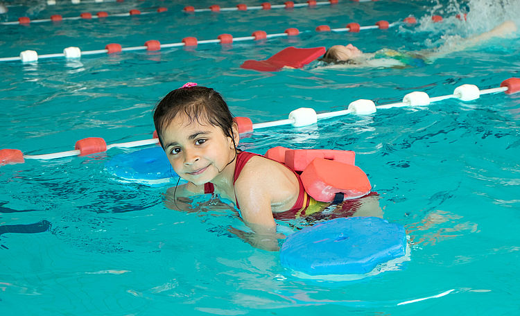 Ein Kleinkind schwimmt mit Schwimmhilfen im Wasser