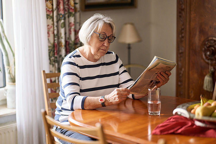Seniorin liest Zeitung an ihrem Küchentisch