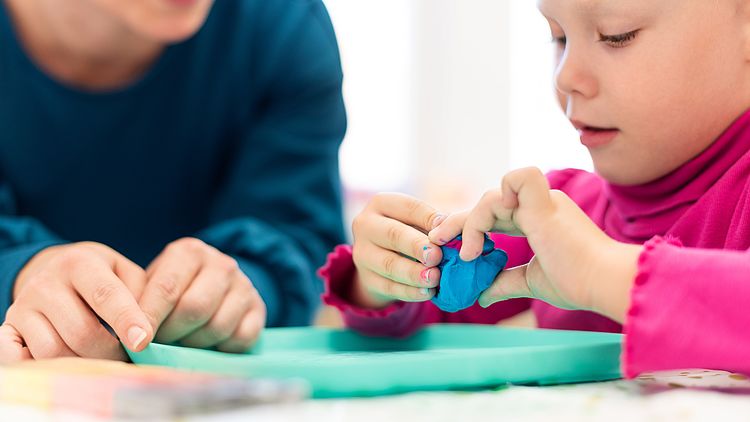 Kleinkind in Ergotherapie-Sitzung, spielerische Übungen mit Knete