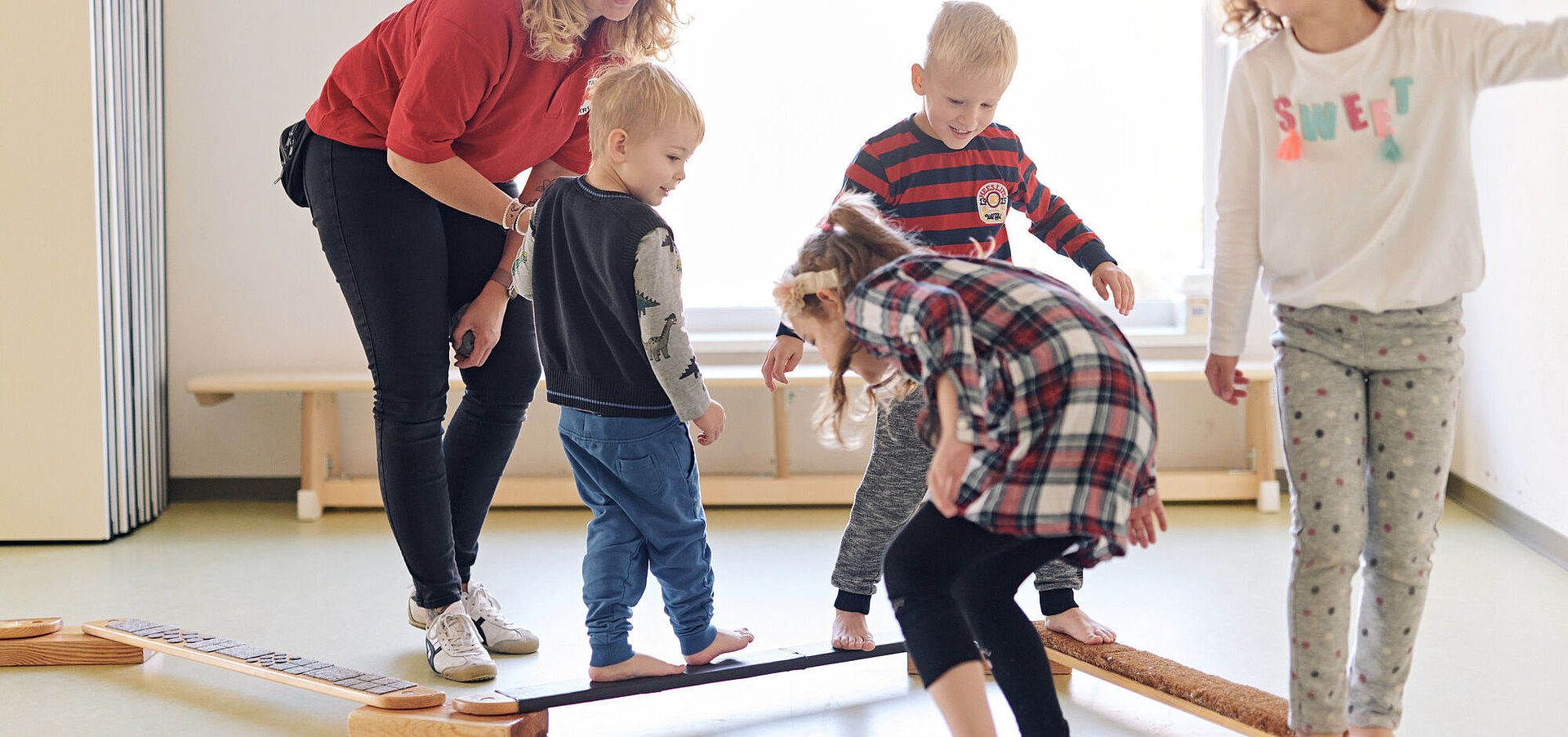 DRK Mitarbeiterin leitet vier Kinder an beim Balancieren im Gymnastikraum
