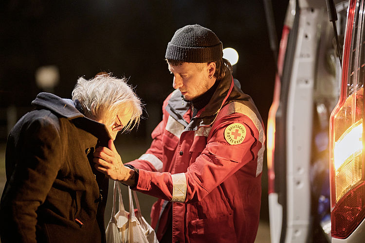 Ehrenamtlicher Helfer des DRK gibt warme Kleidung an Obdachlose aus