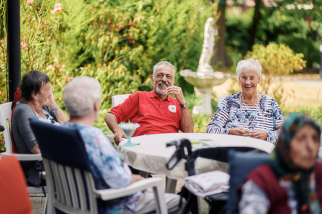 Mitarbeiter des DRK und  Bewohnerinnen beim Eis essen am Tisch auf Terrasse