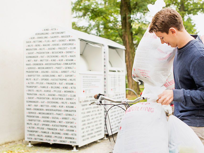 Altkleidercontainer des DRK: junger Mann mit Altkleidersäcken vor Containern des DRK