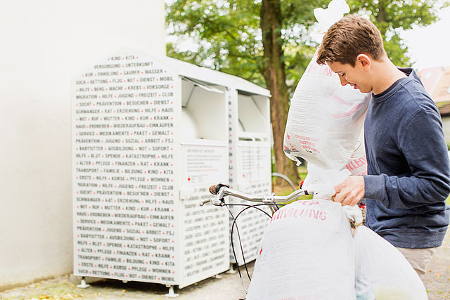 Altkleidercontainer des DRK: junger Mann mit Altkleidersäcken vor Containern des DRK