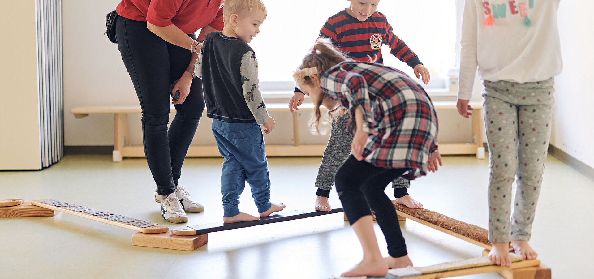 DRK Mitarbeiterin leitet vier Kinder an beim Balancieren im Gymnastikraum