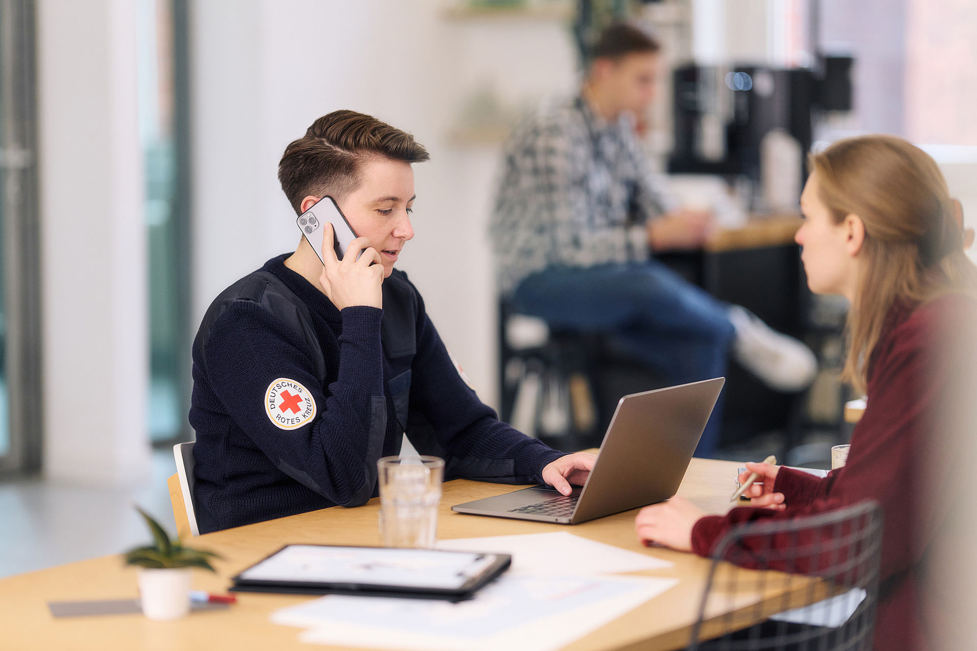 Symbolfoto, Mitarbeiterin des DRK arbeitet am Laptop und telefoniert mit einem Smartphone