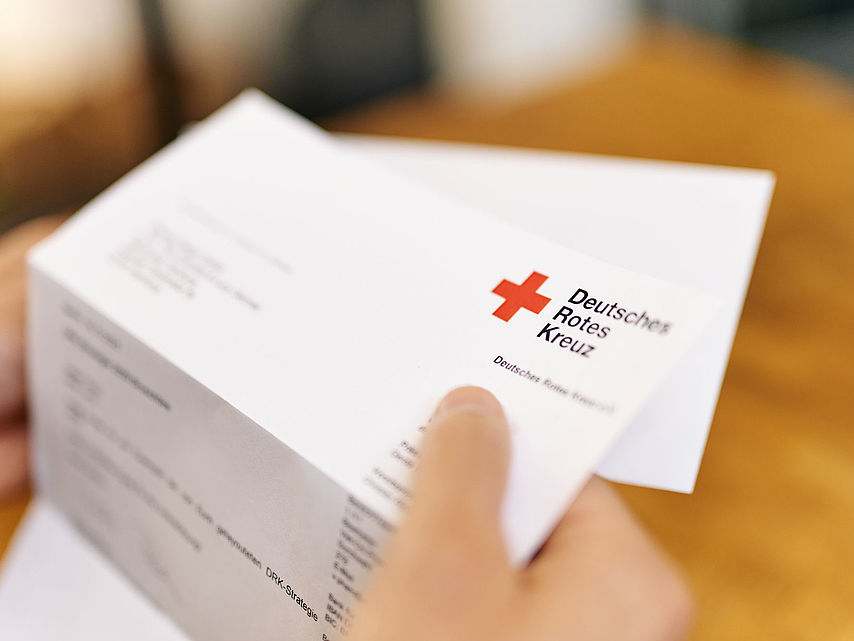 Symbolfoto Brief des DRK. Hand hält Briefbogen mit dem Logo