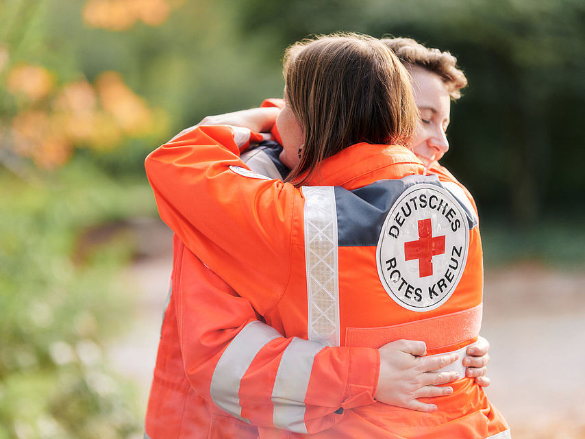 Symbolfoto zwei Kameradinnen in DRK-Einsatzkleidung umarmen sich