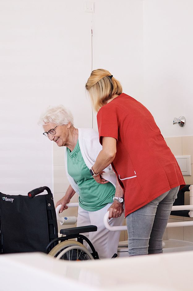 Eine Pflegefachkraft hilft einer älteren Damen in den Rollstuhl