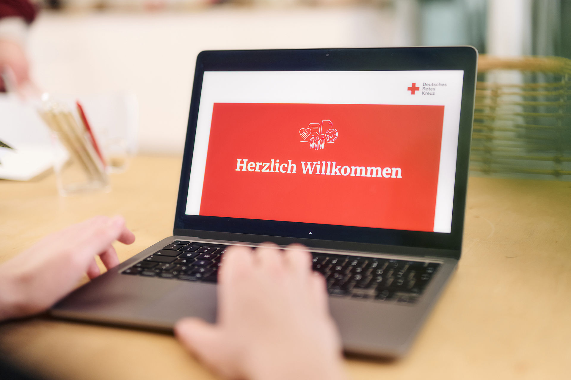 Symbolfoto, das Wort ‚Willkommen‘ und DRK - Logo auf dem Bildschirm eines Laptops